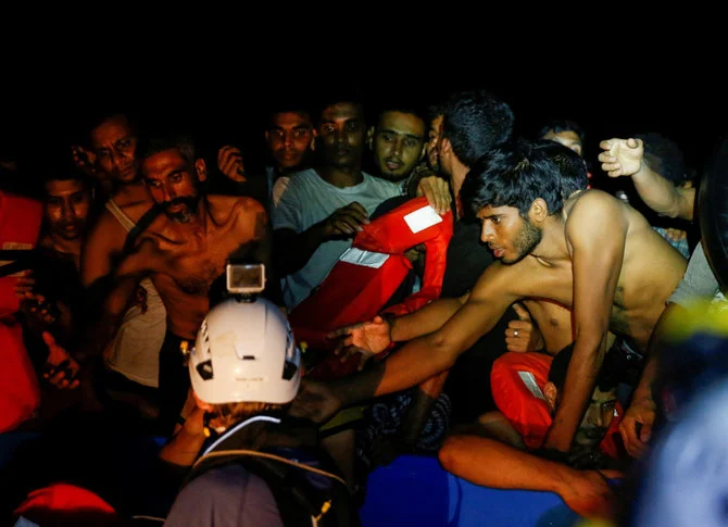 資料写真：地中海西部チュニジア沖の国際海域で、NGO職員が救助活動中にすし詰めの木造船に乗った移民に救命胴衣を配っている（2021年8月1日撮影）。（ロイター）