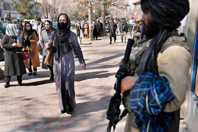 アフガニスタンのカブールでタリバン戦闘員の脇を通るアフガニスタンの女性たち（2022年2月13日撮影）。(AP)