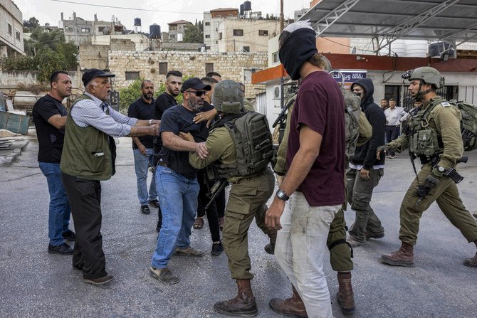 被占領西岸地区の町フワラでの衝突時、パレスチナ人とイスラエル軍兵士がもみ合う横に立つ、覆面をしたイスラエル人入植者。（File/AFP）