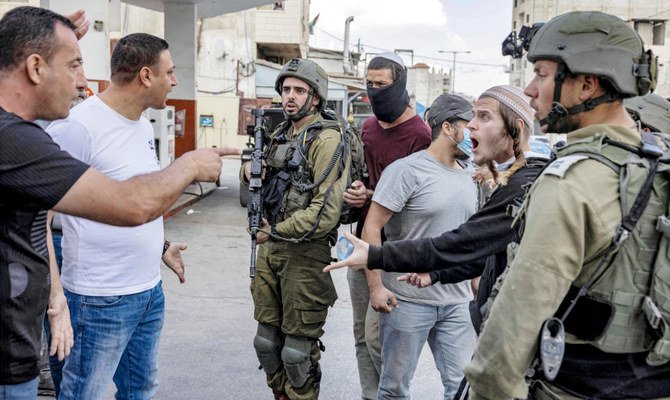 ヨルダン川西岸地区の町フワラで最近発生した衝突の際、兵士が控える中でイスラエル人入植者たちと対峙するパレスチナ人たち。（AFP）