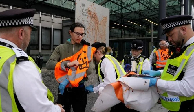 抗議として政府の看板にトマトスープを投げつけて逮捕される「ジャスト・ストップ・オイル」のメンバーたち。2022年10月17日、ロンドン。（写真：AP）