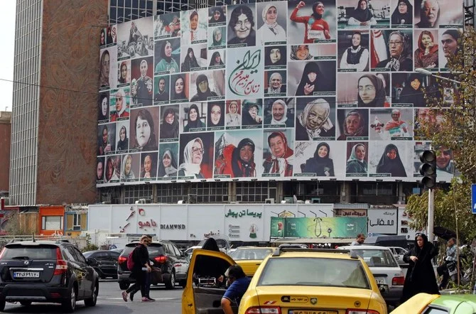 2022年10月13日、テヘランのバリアスル広場で、全員がヒジャブ着用を順守しているイラン人女性をモチーフにした「私の祖国、イランの女性たち」と題したモンタージュ写真をあしらった巨大掲示板の前を、車で通るイランの人々。（AFP）