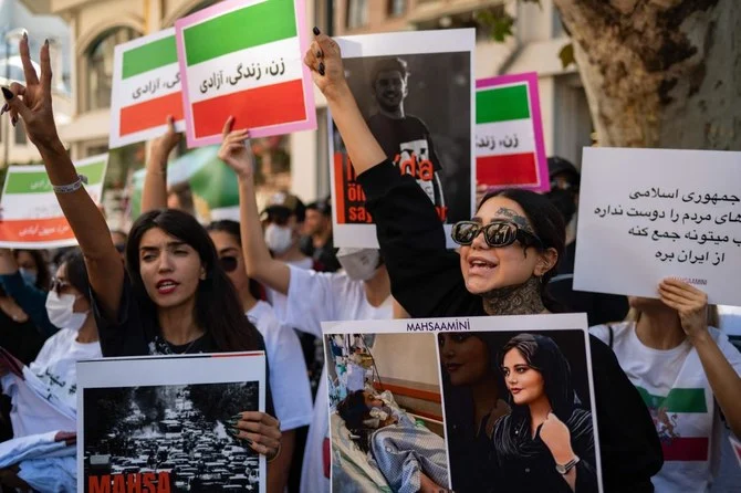 2022年9月29日、イスタンブールのイラン領事館前で行われた集会に参加し、イラン人のマフサ・アミニ氏の肖像が描かれた横断幕を手にスローガンを叫ぶデモ参加者たち。（AFP）