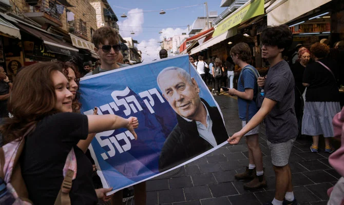 イスラエルの元首相でリクード党首のベンヤミン・ネタニヤフ氏の選挙ポスターと一緒に写真撮影する人々。イスラエルの国政選挙前日の2022年10月31日（月）、エルサレムのマハネ・イェフダ市場。（AP）