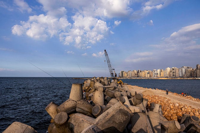 港の海岸に沿って設置されているコンクリートブロックの間に立って釣り竿を使う人々。エジプト北部の沿岸都市アレクサンドリア。（ファイル/AFP）