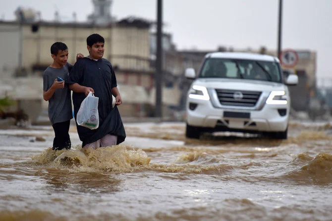 2022年11月24日、ジェッダで大雨が降り、フライトが遅れ、学校が休校となり、メッカに通じる道路が閉鎖された後、浸水した道を歩く若者たち。（AFP）