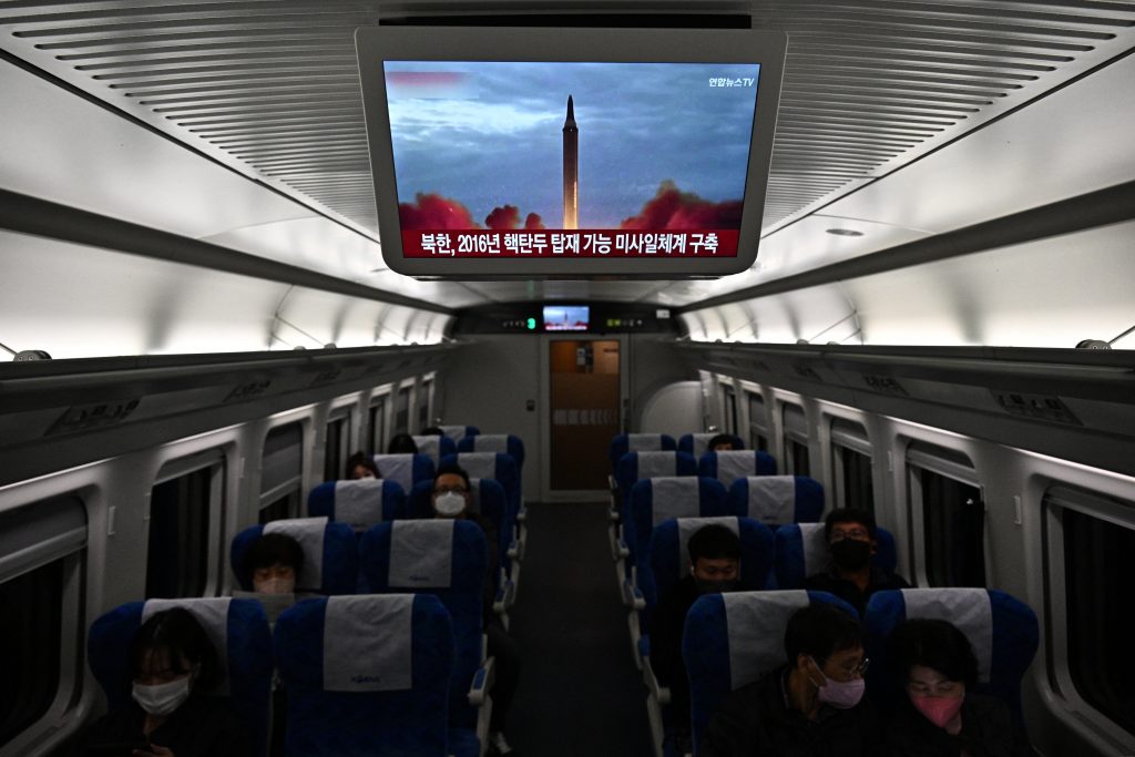 2022年11月2日、ソウル郊外にて、北朝鮮によるミサイル発射実験の資料映像が流れるニュース放送が映るテレビの下、電車内に座っている通勤客。（AFP）