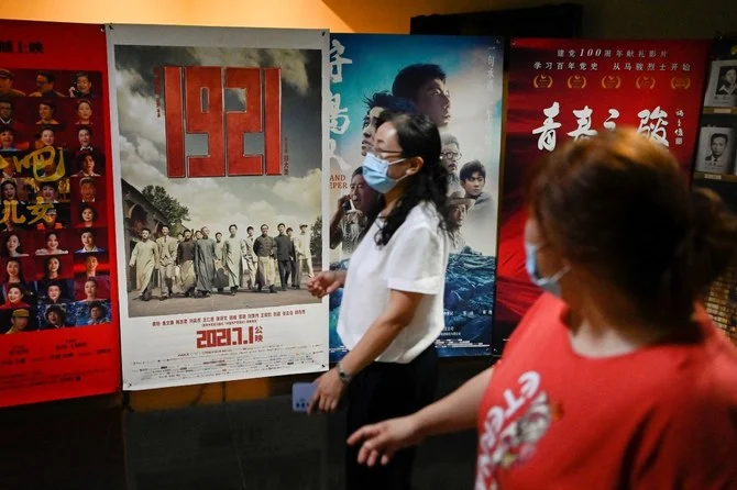 1921年の中国共産党創立を描いた映画「1921」のポスターの前を通り過ぎる人々。同党創立100周年記念日を前にした2021年6月28日、北京の映画館。（ファイル/WANG Zhao/AFP）