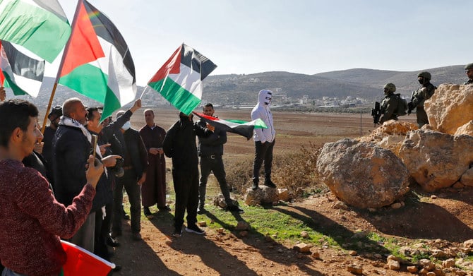 パレスチナ人たちが国旗を振りながらイスラエルの基地建設に反対するデモをする中、位置に付くイスラエル治安部隊。2022年12月2日、ヨルダン川西岸地区のナブルスの東にあるベイト・ダジャン。（AFP）