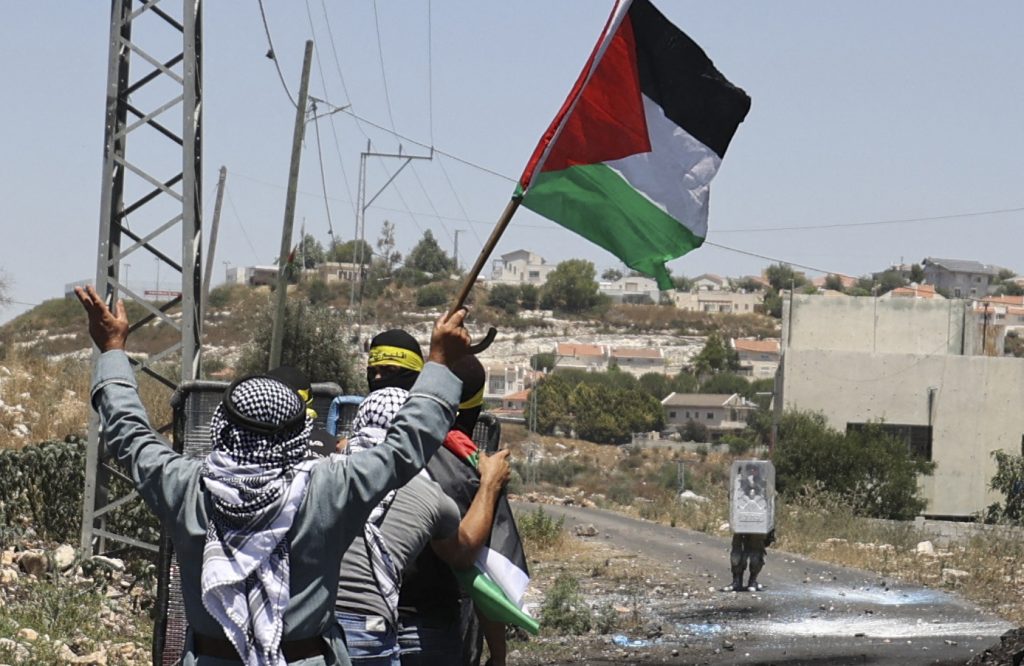 イスラエルによるパレスチナの土地の収奪に対する抗議行動後のイスラエル軍との衝突中に国旗を掲げる高齢のパレスチナ人男性。(AFP)