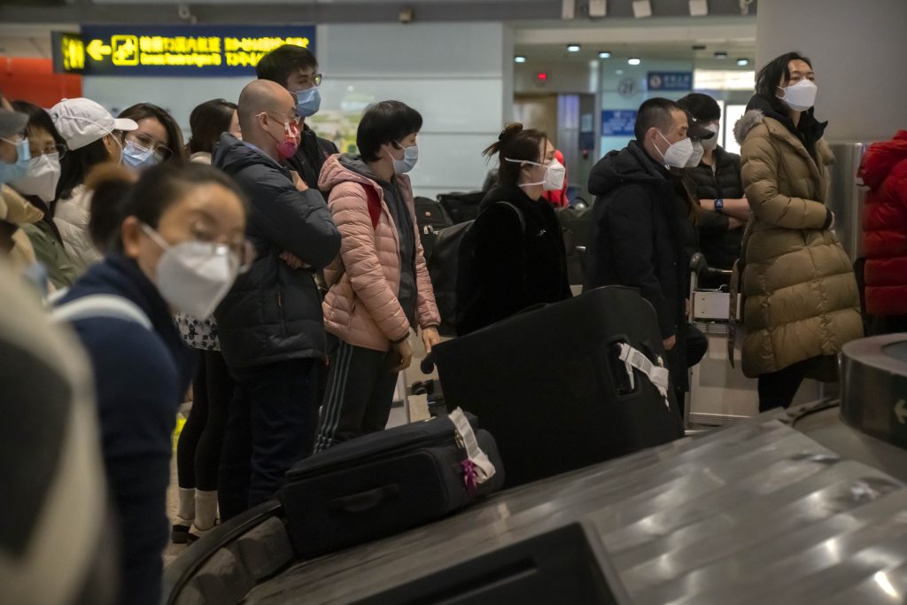 2023 年 1 月 9 日、マスクを着用した旅行者たちが北京首都国際空港の国際線到着エリアで荷物を待っている。（ファイル／AP）