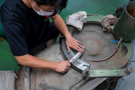 2022年9月2日撮影、岐阜県関市にあるスミカマの工場で、最終工程で回転する砥石を使って包丁を仕上げる作業員の様子。（AFP）