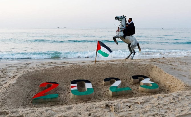 パレスチナ人が人命損失という意味で悲痛な年だった2022年に別れを告げようとしていたこの年最後の日没時、砂浜で2023という数字を象った砂の彫刻の横で馬に乗る男性。2022年12月31日、ガザ地区。（ロイター）