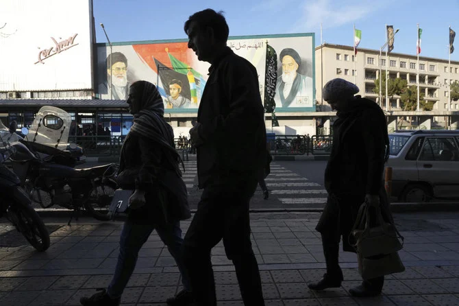 イランの首都テヘランの情景と風になびくイラン国旗。2023年1月7日。(AFP) テヘランのダウンタウンのエンケラブ・エ・エスラミ (イスラム革命) 通りで、イラン革命を成し遂げた故ホメイニ師 (右) と最高指導者ハメネイ師 (左) 、バジ軍の壁画の前を歩く歩行者たち。2023年1月7日。(AP)