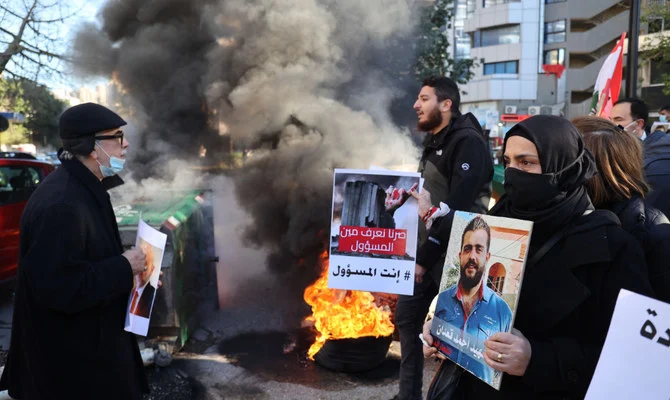 2020 年 8 月 4 日に起きたベイルート港爆発事故の犠牲者のレバノン人血縁者たちが、2022 年 1 月 17 日にベイルートの正義宮殿の外で座り込み中に故人の写真を手に持ち、他の人たちがタイヤに火をつけている。（AFP）