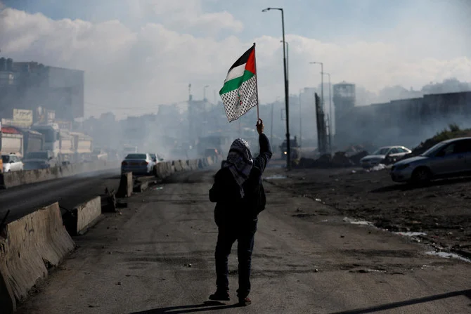 パレスチナ人が抗議デモでイスラエル軍と衝突する中、パレスチナ国旗を持って歩く男性（ロイター）