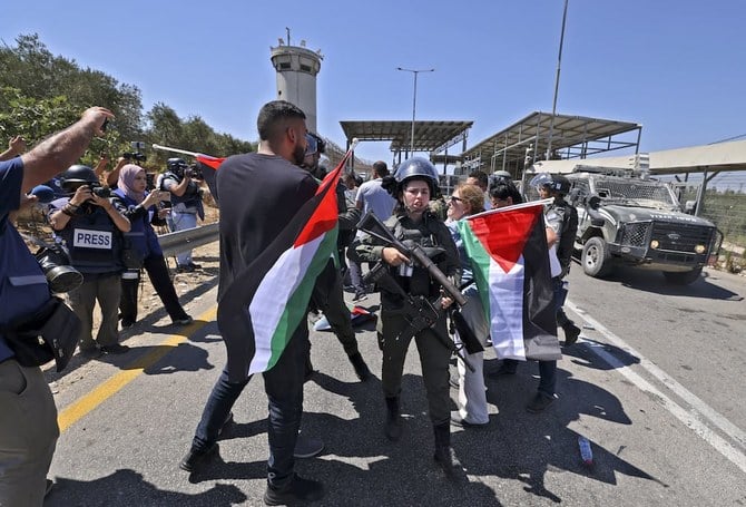 ユダヤ人入植地反対デモで、パレスチナ国旗を掲げてイスラエル治安部隊と対峙するパレスチナ人たち。（AFP）