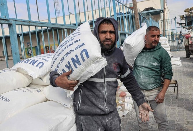 ガザ地区南部のラファ難民キャンプにある国連パレスチナ難民救済事業機関（UNRWA）の配送センターで、貧しい家族への援助として受け取った小麦粉の袋を運ぶパレスチナの人々（AFP通信）