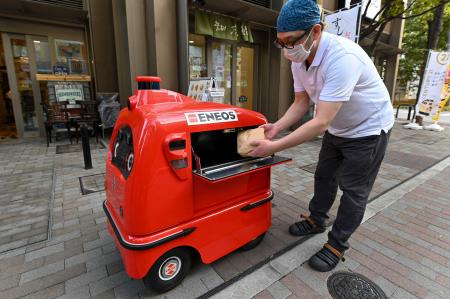 2023年1月18日、東京都内で、東京を拠点とするロボットメーカーのZMPが開発した配達ロボット「デリロ」が配達用の食品袋を受け取る様子を撮影した写真。(AFP)