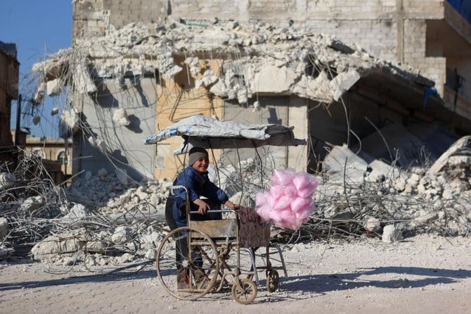 シリアのアレッポ県、反政府派が支配するアタリブ村で、先週発生した地震で倒壊した建物の前で綿菓子を売りながら笑顔を見せるシリア人の子供。2023年2月14日（AFP）