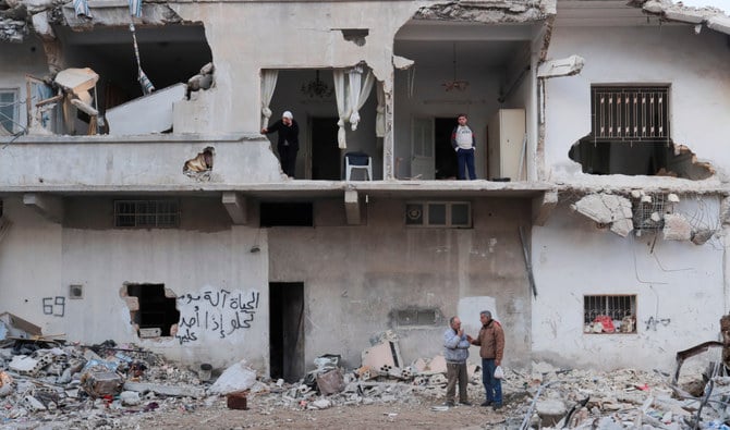 15日、シリアのジャブラで友人と話す72歳のガッサン・リハウィ氏（左下）。彼の家族が地震で壊れた家の中に立っている。（ロイター）