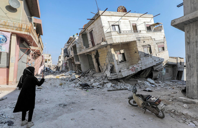 シリア北西部ジンディレスで、狭い道路沿いにある倒壊した建物を、女性が携帯電話を使って撮影している。この建物は、2月6日にシリアとトルコを襲った、死者を出した地震の余波で倒壊した。（2023年2月19日撮影）（AFP）