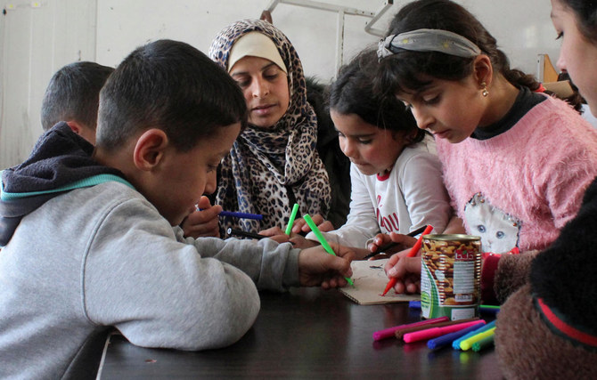 シリアのラタキアで、大地震による被災家族のための避難所となった学校で、3人の子どもの母親(39歳)が子どもたちと一緒に座っている。(ロイター)