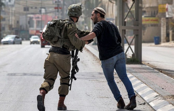 兵士と言い争うイスラエル人入植者＝2023年2月27日、ヨルダン川西岸地区ナブルス市近郊の町フワラ（AFP）