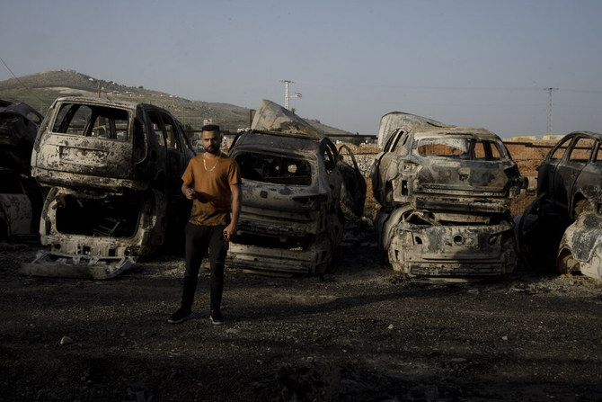 2023年2月28日（火）、ヨルダン川西岸地区ナブルスの近くにあるハワラで、パレスチナ人男性が、入植者の暴動で放火された車の間に立ち、たばこを吸っている。（AP）