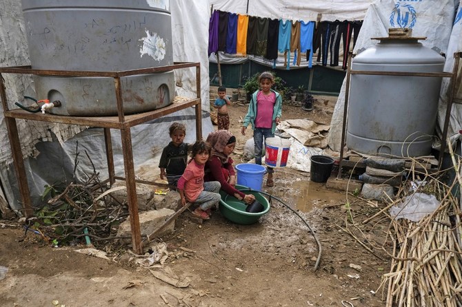 レバノン北部のアッカール県タルハヤトにあるシリア難民の仮設キャンプで、テントの外でプラスチック容器に入れた食器を洗う女性と、その側に居続ける子どもたち。（AFP）