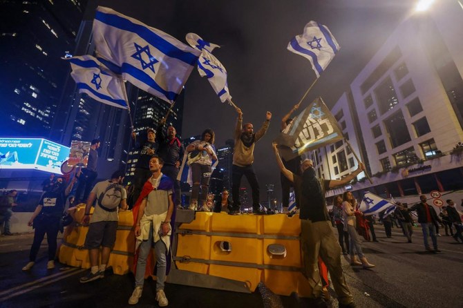 テルアビブで、議論を呼んでいる政府の司法制度抜本改革法案に反対する集会中、道路を塞ぐバリケード上で国旗を振るイスラエルのデモ隊。2023年3月25日。（AFP）