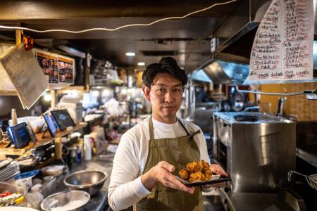こちらの写真は2023年3月14日に撮影され、東京の蒲田にある居酒屋でまつもとたけひろさんが、唐揚げが盛られた皿を持ってポーズをしている。（AFP）