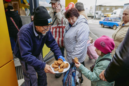 日本から来た75歳の人道支援ボランティアの土子文則氏。自身で開くカフェの外で女児にクッキーをふるまう。2023年4月24日、ウクライナ、ハルキウで。（ロイター）