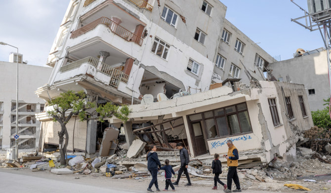ケナン・チヴィさんとその家族は、2023年2月6日にトルコ南東部を襲ったマグニチュード7.8の地震の後、「私たちは戻ってくる」と書かれた破損した家の前に集った（3月28日、ハタイで）。 (AFP)