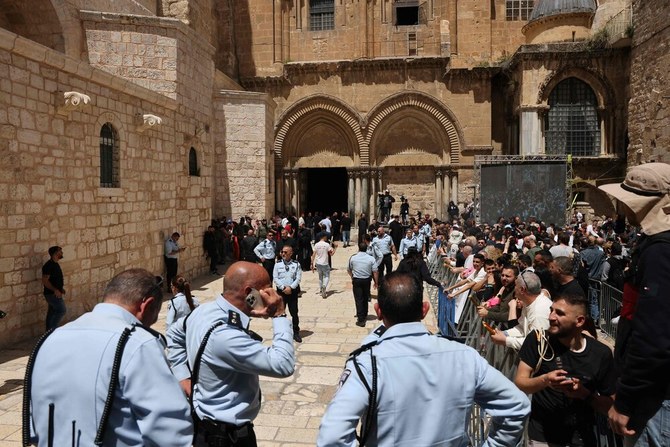 2023年4月15日、正教会のイースターサタデーの祝祭中、エルサレム旧市街の聖墳墓教会の入り口に立つイスラエルの治安部隊と、治安部隊が設置したフェンスの後ろで待つキリスト教の礼拝者たち。（AFP）
