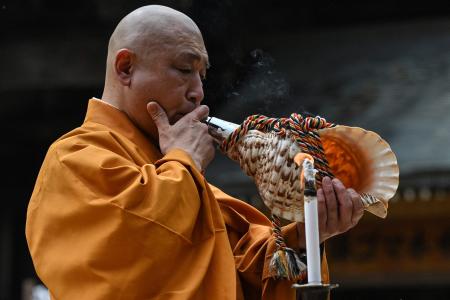 2023年5月14日に撮影されたこの写真には、広島の近くにある宮島の仏教寺院大聖院にて、数千羽の折り鶴をお焚き上げする際に法螺貝を吹いている三松庸裕氏が写っている。  （AFP）