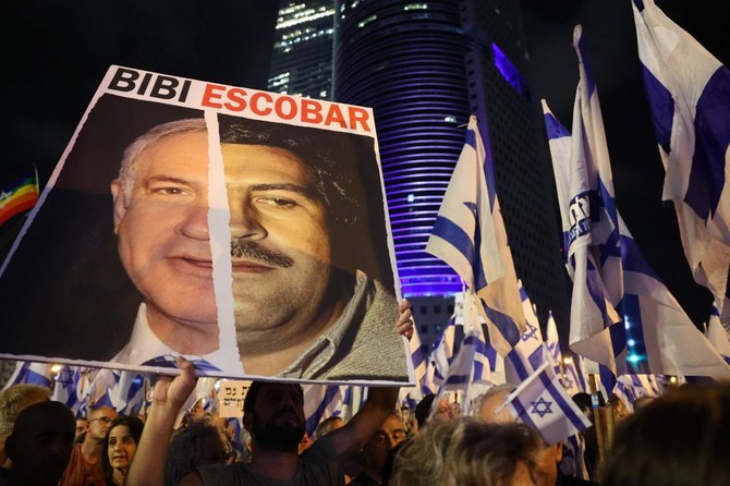 物議を醸している強硬右派政権の司法改革計画に対するデモが行われる中、イスラエルのベンヤミン・ネタニヤフ首相と麻薬王の故パブロ・エスコバル氏の写真を載せたプラカードを掲げる男性。2023年6月10日、テルアビブ。（AFP）