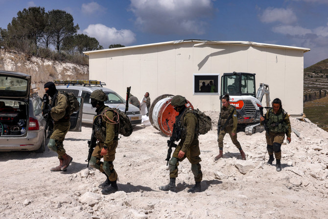 占領下のヨルダン川西岸地区内の前哨入植地ホメシュで、設置中の移動式建物の外を歩くイスラエル人兵士ら。2023年5月29日。（写真：メナヘム・カハナ / AFP）