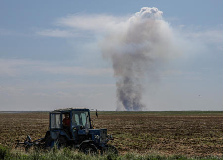 2023年6月20日、ウクライナのヘルソン州で、ロシアによるウクライナ攻撃のさなか、軍事攻撃後遠くに煙が立ち込める中、トラクターを運転する農業従事者。（ロイター/ファイル）