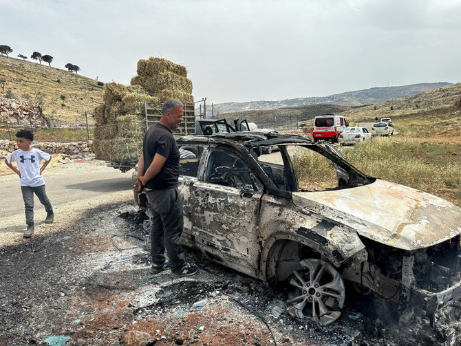 イスラエルが占領したヨルダン川西岸のラマッラー付近で起きた衝突の際に、イスラエル入植者によって焼かれた車を調べているパレスチナ人。（ロイター）