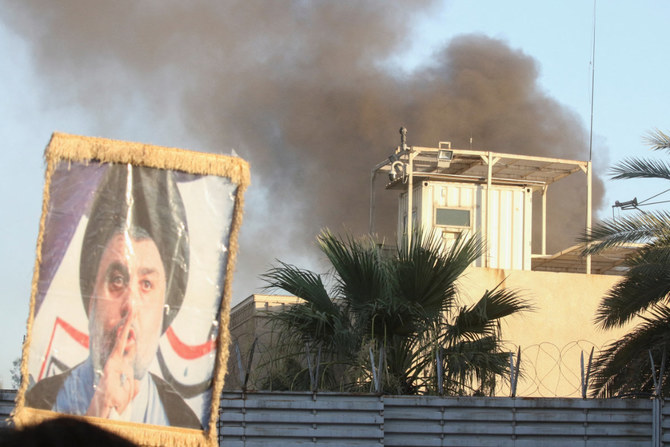 2023年7月20日の抗議中、ある抗議者がイラクのシーア派指導者ムクタダー・アル・サドル氏の肖像を掲げる中、スウェーデン大使館の建物からは煙が上がる。（ロイター）
