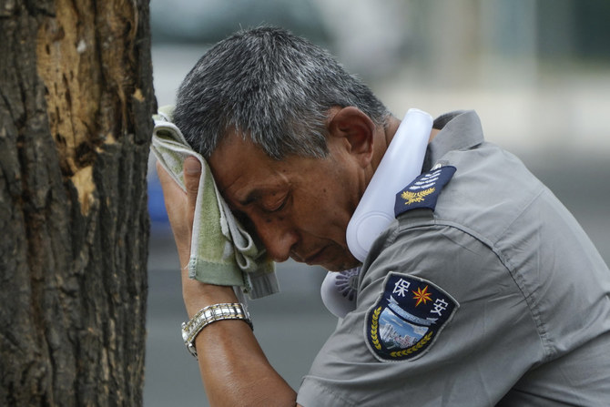 暑さの中、汗を拭う、首に扇風機をつけた警備員＝2023年7月3日、中国・北京。（AP）