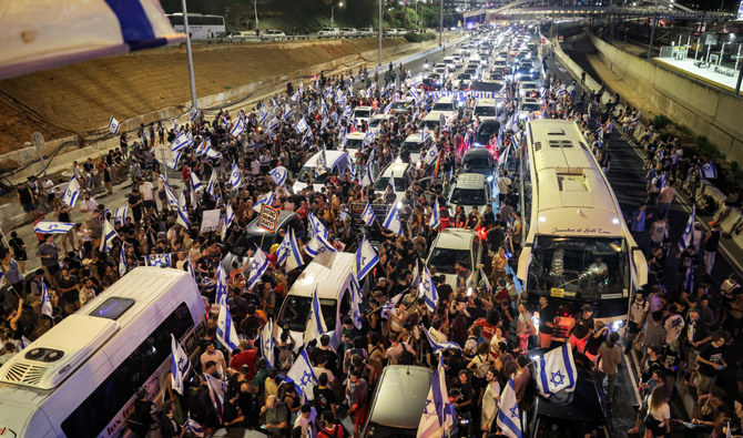 イスラエル政府の司法改革計画に対する抗議集会の最中、走行中の車の間に立って幹線道路を封鎖するデモ隊。2023年7月24日、テルアビブ。（AFP）