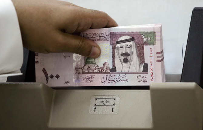 サウジのアブドゥラー・ビン・アブドルアジーズ・アール・サウード国王の肖像入りの新しい100リヤル札を数える同国の銀行員。2007年6月5日、リヤドの銀行。（AFP）