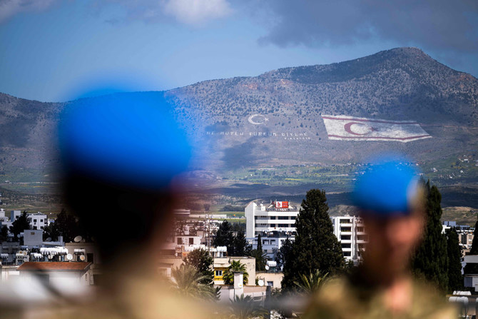 キプロスの首都ニコシアを二分する国連緩衝地帯にあるレドラ宮殿の屋上に立つ国連平和維持軍兵士たち。後景には島北部のキレニア山脈の山腹に描かれた、自称国家である北キプロス・トルコ共和国（TRNC）の国旗が見える。2023年4月5日。（AFP）