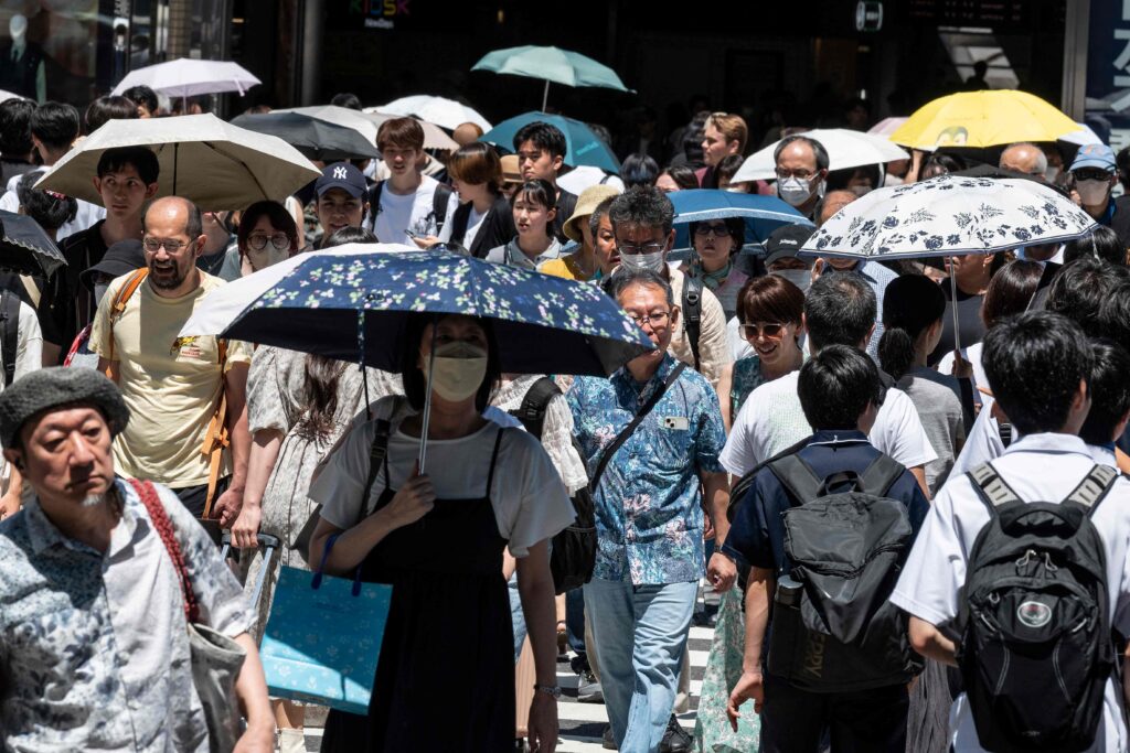 2023年7月30日撮影のこの写真は、35度を超える気温が首都東京で数週間にわたり続く中、熱気から逃れようと傘やパラソルを差して新宿駅の外を歩く人々の様子である。（AFP通信）