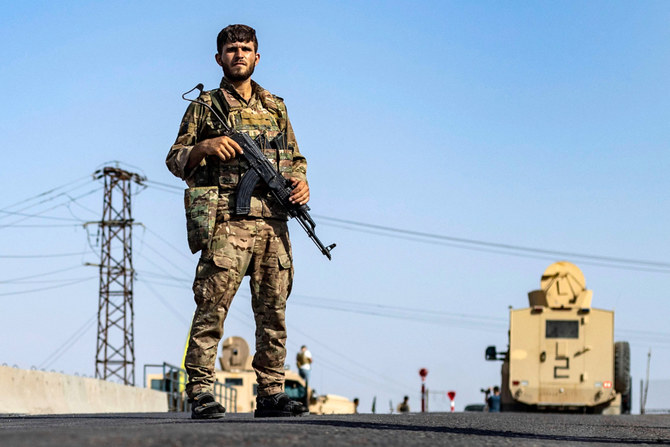 シリア北東部デリゾール州のアルバセイラの町で、シリア民主軍(SDF)主催のメディア向けガイドツアー中、道路沿いで警備に当たるSDF戦闘員。他の兵士は夜間外出禁止令を発令するために配置に就いている。2023年9月4日。(AFP通信)