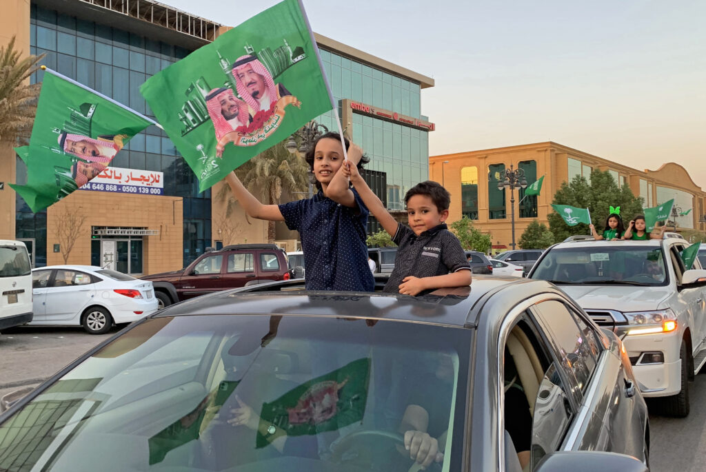 2020年9月23日、サウジアラビアの建国記念日を祝うリヤドで、サウジアラビアのサルマン・ビン・アブドゥルアズィーズ国王と息子のムハンマド・ビン・サルマーン皇太子の写真入りの国旗を振る少年たち。(AFP＝時事）