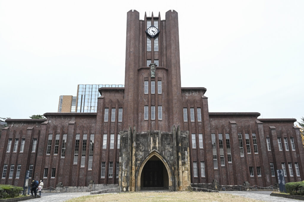 2022年12月17日撮影、東京にある東京大学本郷キャンパスの中心にある1925年竣工の安田講堂の隣の看板を見る人々（左）。（Richard A. Brooks撮影 / AFP）