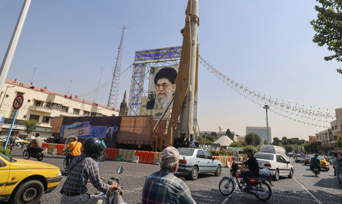 アヤトラ・アリー・ハメネイ最高指導者の肖像画と並ぶイランの地対地ミサイル、セッジールの前をバイクで通り過ぎる人々。9月30日、デモ隊が1年前に同じ地域で抗議デモに参加して殺害された数十人を追悼する中で、治安部隊が数十名を逮捕した。（AFP）
